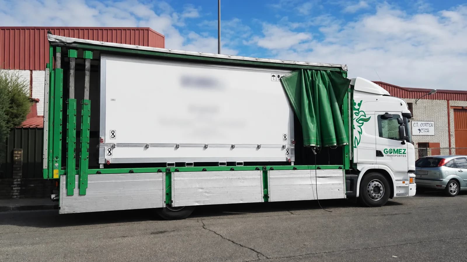 Contenedor industrial blanco cargado en un camión de lona con los laterales abiertos